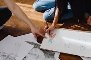 Close-up of hands sketching fashion designs on paper indoors.