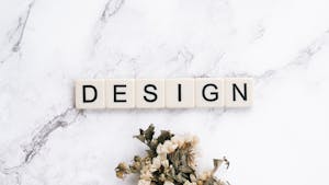 Close-up of Scrabble tiles spelling 'design' on marble with flowers.